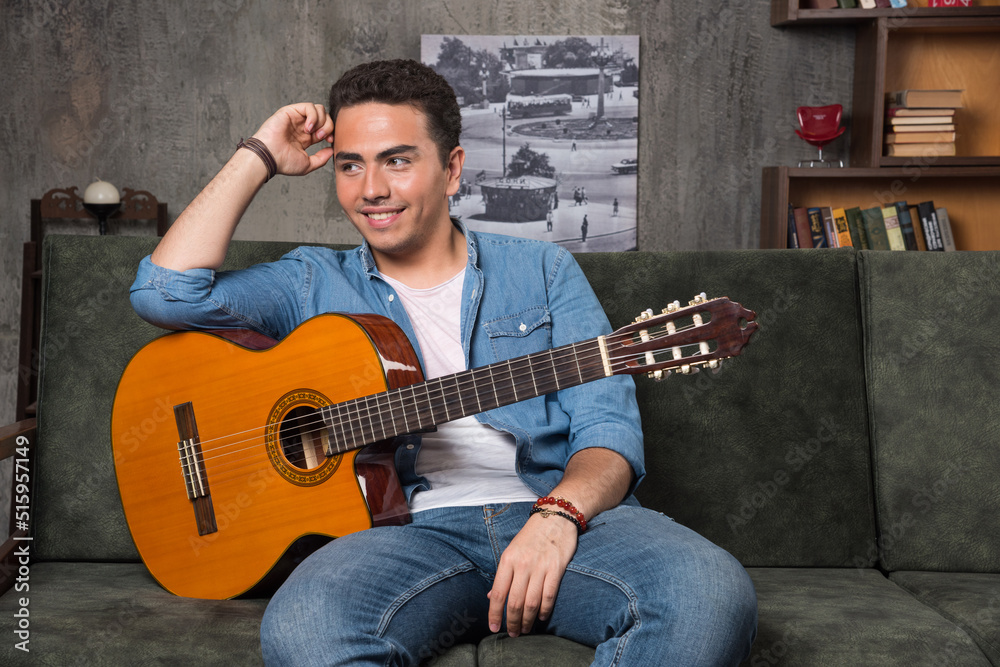 Obraz premium Young musician holding a beautiful guitar and sitting on sofa
