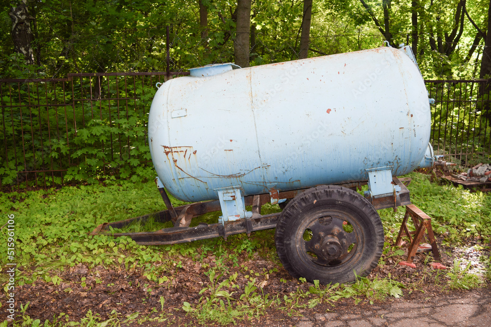 An old blue metal container on the road near the fence on a summer day An old blue metal container on the road near the fence on a summer day