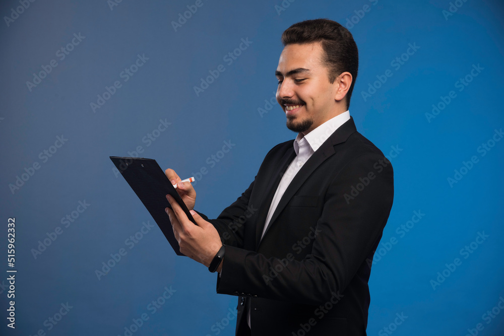 Businessman in black suit holding the tasklist and taking notes Businessman in black suit holding the tasklist and taking notes