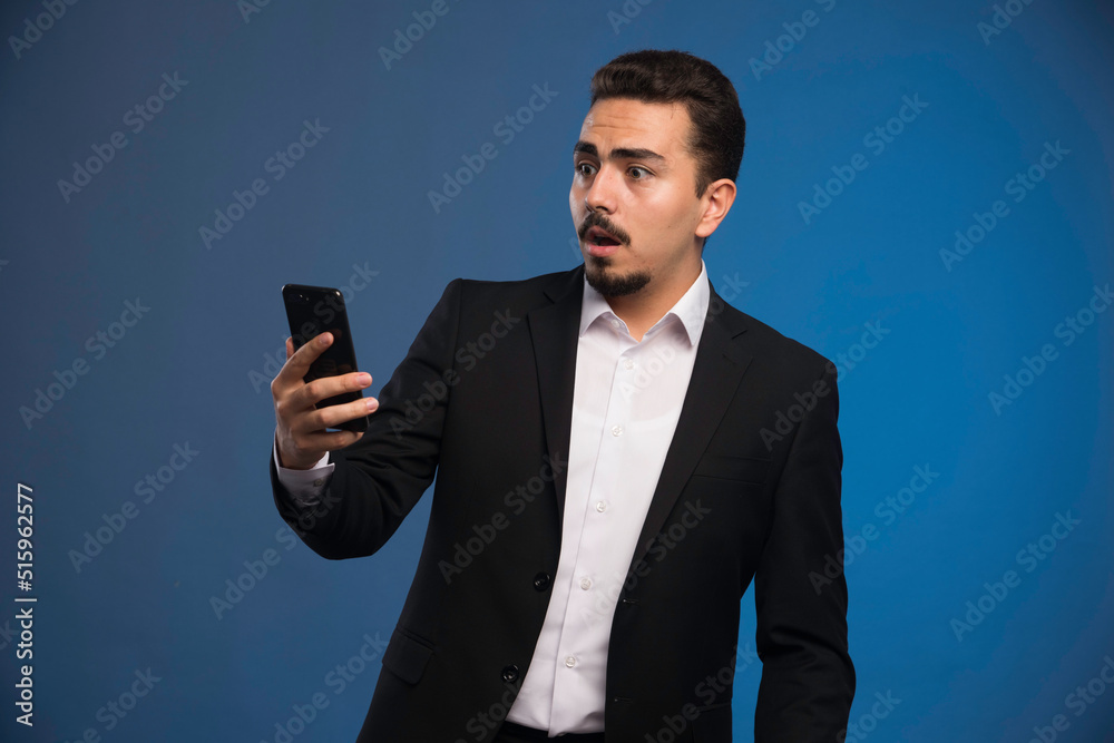 Businessman in black suit checking his telephone and surprized Businessman in black suit checking his telephone and surprized
