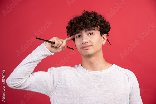 Young male artist looking at camera with painting brushes