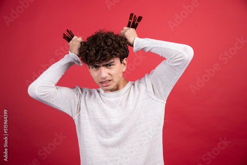 Young painter angrily holding brushes on red background
