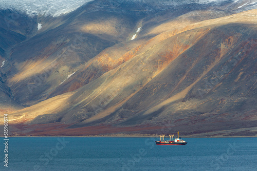 Cargo ship in the bay. Epic arctic landscape. Beautiful mountains on the coast. Sea freight and supply in the North-East of Russia. Egvekinot Bay, Kresta Gulf, Bering Sea. Chukotka, Russian Far East. photo