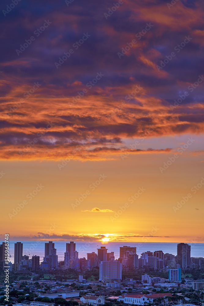 A sunset over a city skyline near the sea with cloudy purple and orange sky. Sunrise over a blue horizon near urban landscape with copy space. Peaceful holiday destination at night in Waikiki, Hawaii