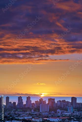 A sunset over a city skyline near the sea with cloudy purple and orange sky. Sunrise over a blue horizon near urban landscape with copy space. Peaceful holiday destination at night in Waikiki, Hawaii