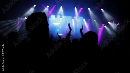 People at music rock concert. Silhouettes of happy people raising their hands. Crowd at performance, blurred stage lights. Lot of hands during the live concert, bright stage lights