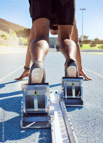 Feet of athlete in starting position on a running track. A male track and field runner ready to leave the starting block to start his sprint. Sportsman with hands on the starting line during a race