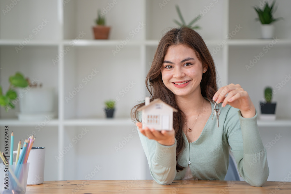 Woman holding white house model and house key in hand.Mortgage loan approval home loan and insurance concept. Woman holding white house model and house key in hand.Mortgage loan approval home loan and insurance concept.