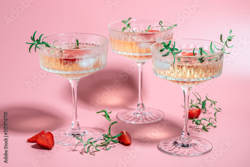 drink cocktail with ice in a glass on pink background. refreshing fruit cocktail or punch with wine champagne, strawberries, ice and rosemary