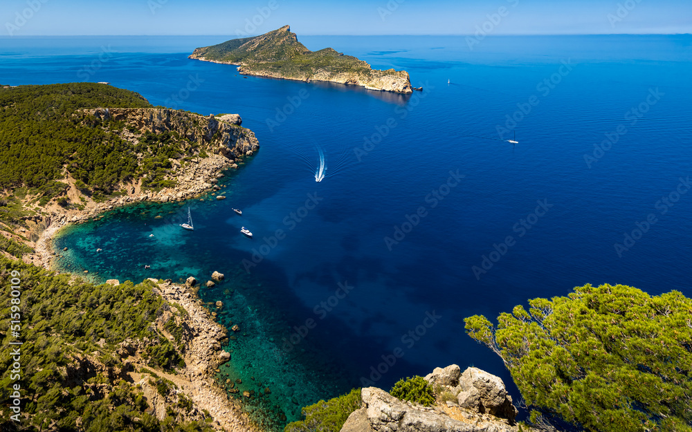 Panorama view from a cliff of the rocky coastline of idyllic Mallorca cove Cala en Basset nearby Sant Elm with boats and the island Sa Dragonera with the mountain Puig des Aucells in the background.