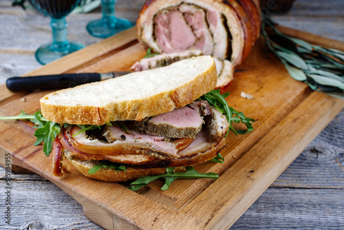 Traditional barbecue Italian porchetta pork belly roll meat sandwich with rocket salad served as close-up on a rustic wooden board photo