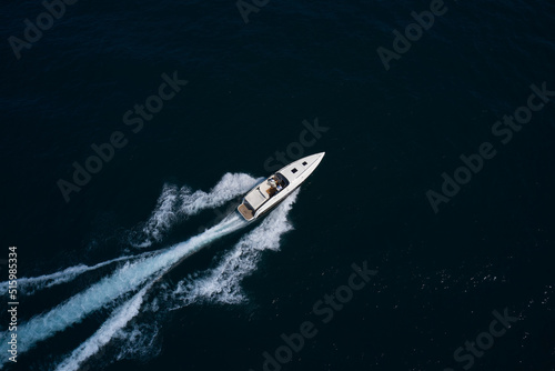 Big speedy white boat with two people moving fast on dark water aerial view. © Berg