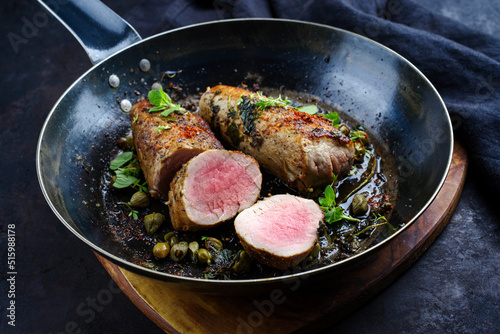 Traditional fried duroc pork fillet pieces with capers and spices served as close-up in a rustic skillet