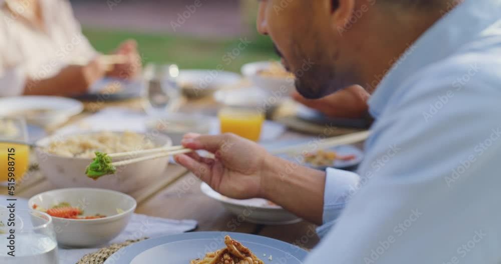 An asian man eating a meal with his family using chopsticks..Young man having lunch or dinner at a function or gathering in an outdoor dining area. A healthy, delicious meal shared together An asian man eating a meal with his family using chopsticks..Young man having lunch or dinner at a function or gathering in an outdoor dining area. A healthy, delicious meal shared together