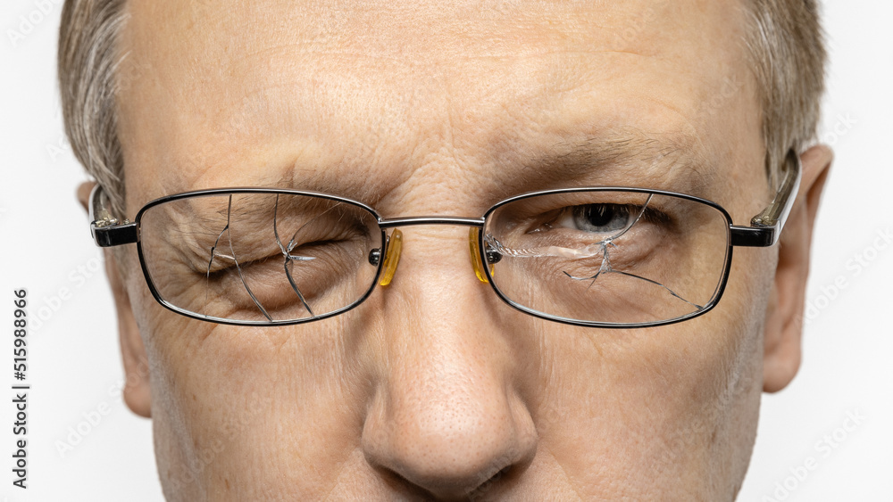 A middle-aged man in glasses with broken lenses, one eye is closed. Portrait, studio shot. A middle-aged man in glasses with broken lenses, one eye is closed. Portrait, studio shot.