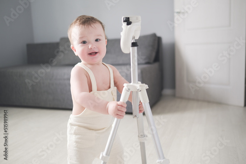 Cute toddler boy in overalls playing with tripod for photos