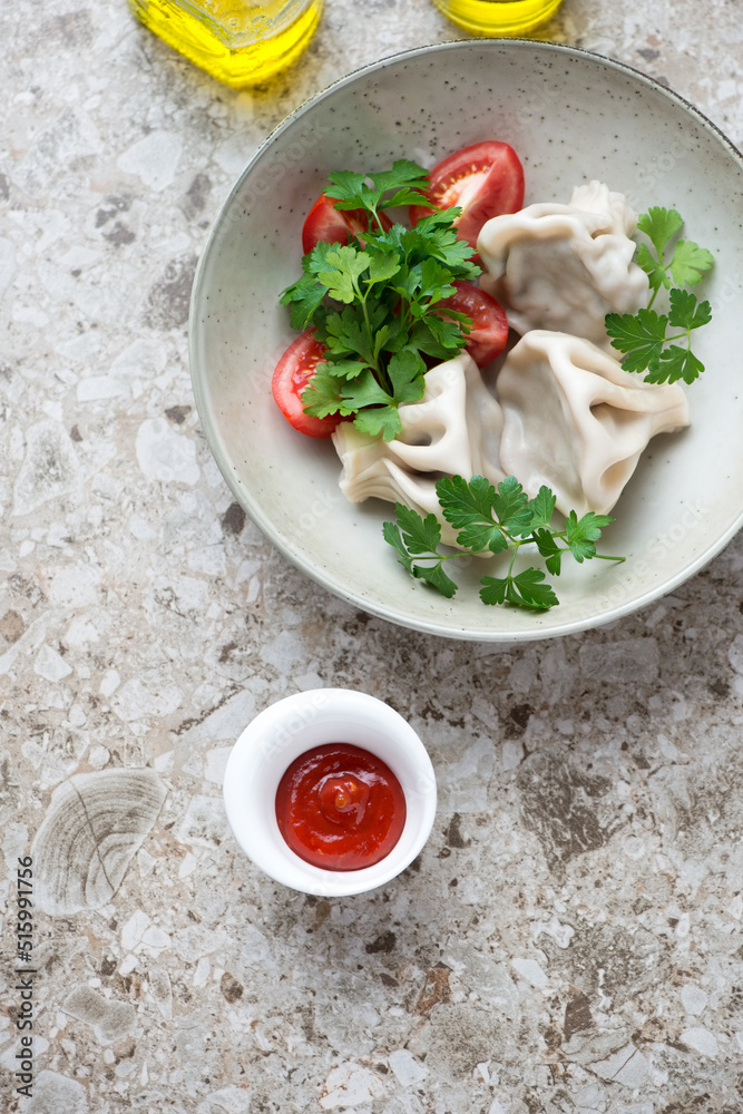 Plate of georgian meat dumplings khinkali with fresh parsley and tomatoes, flat lay on a brown granite background, vertical shot Plate of georgian meat dumplings khinkali with fresh parsley and tomatoes, flat lay on a brown granite background, vertical shot