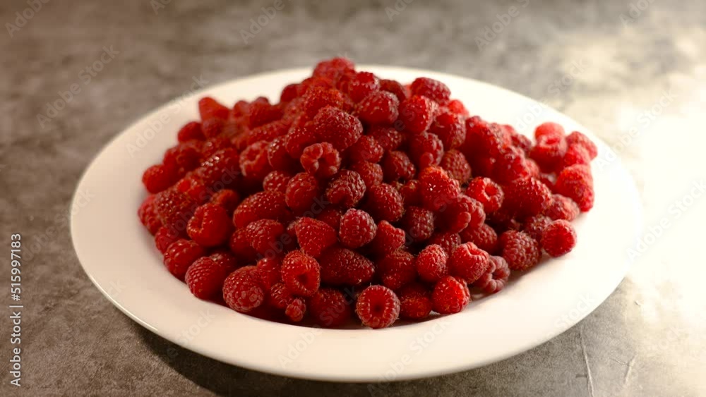 White plate of ripe raspberries on stone table White plate of ripe raspberries on stone table
