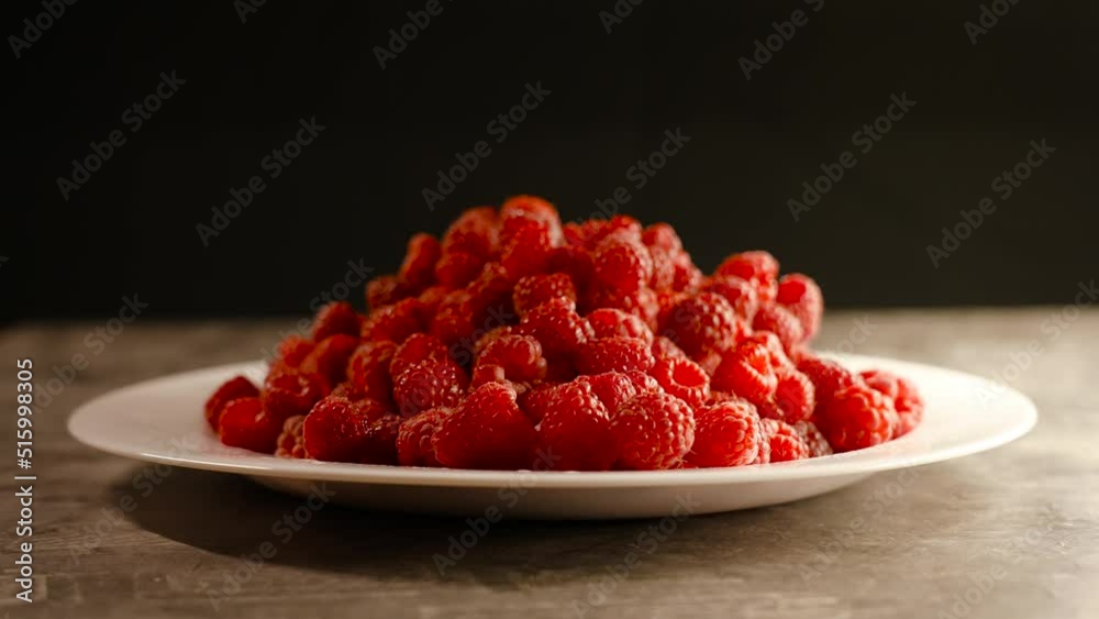 White plate of ripe raspberries on stone table White plate of ripe raspberries on stone table