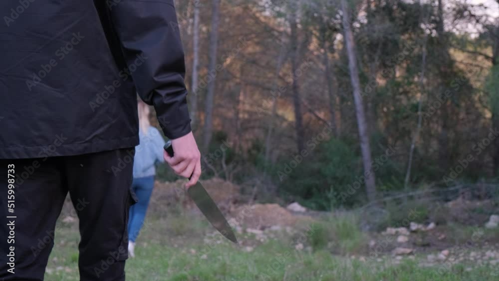 A man with a knife in the forest. The maniac pursues the victim and prepares to attack. The girl runs away from the killer A man with a knife in the forest. The maniac pursues the victim and prepares to attack. The girl runs away from the killer