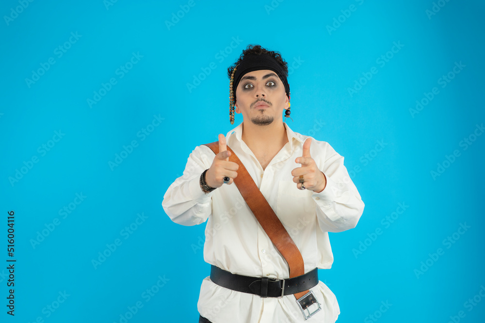 Handsome pirate point fingers to the camera and stand on blue background. Handsome pirate point fingers to the camera and stand on blue background.