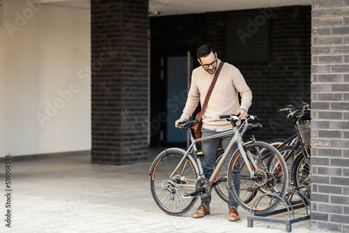 A casual businessman parking his bicycle outdoors.
