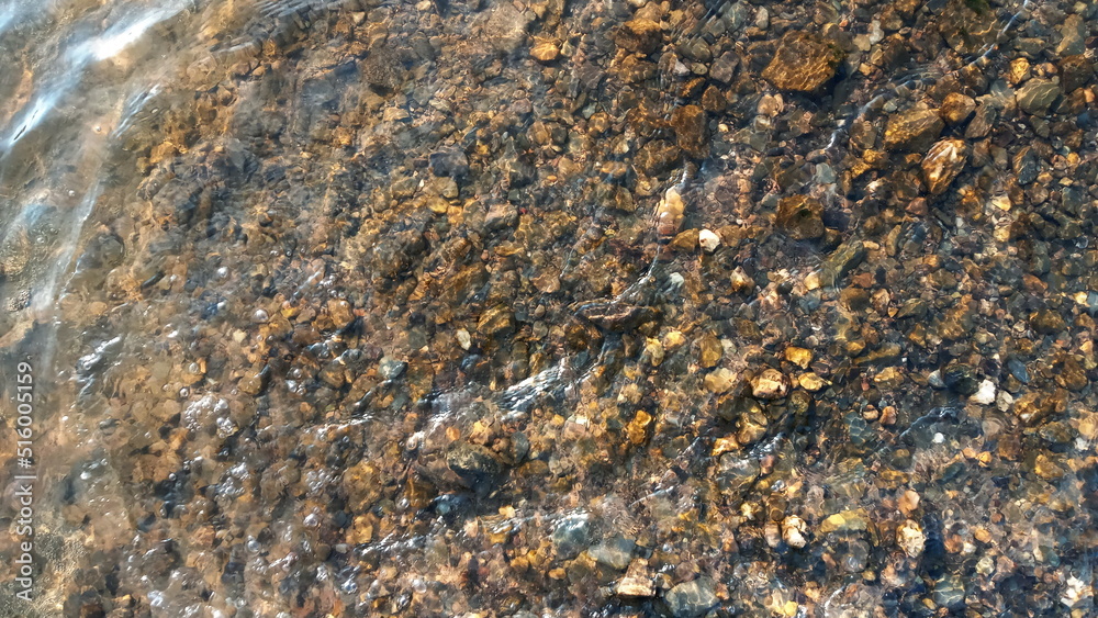 Top view on colorful pebbles covered by water. Close up view of smooth round pebble stones on the beach. Top view on colorful pebbles covered by water. Close up view of smooth round pebble stones on the beach.