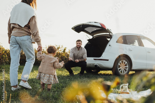 Young Family Enjoying Road Trip, Mother and Father with Little Daughter Outdoors Having Picnic with SUV Car on the Background