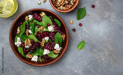 Beet or beetroot salad with baby spinach, cheese, nuts, cranberries on plate with fork, dressing and spices on gray background, top view. place for text