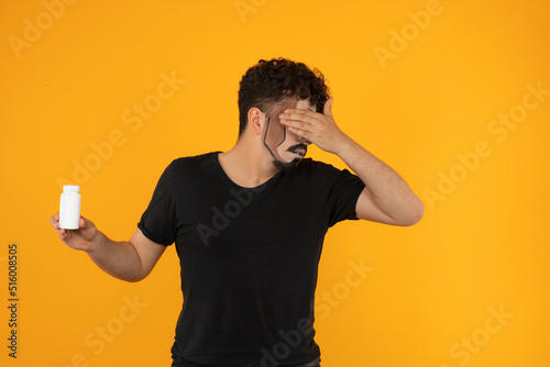 young man holding pill case and hide his face with his hand