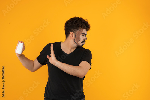 Young creative man saying no to the pills and stands on orange background