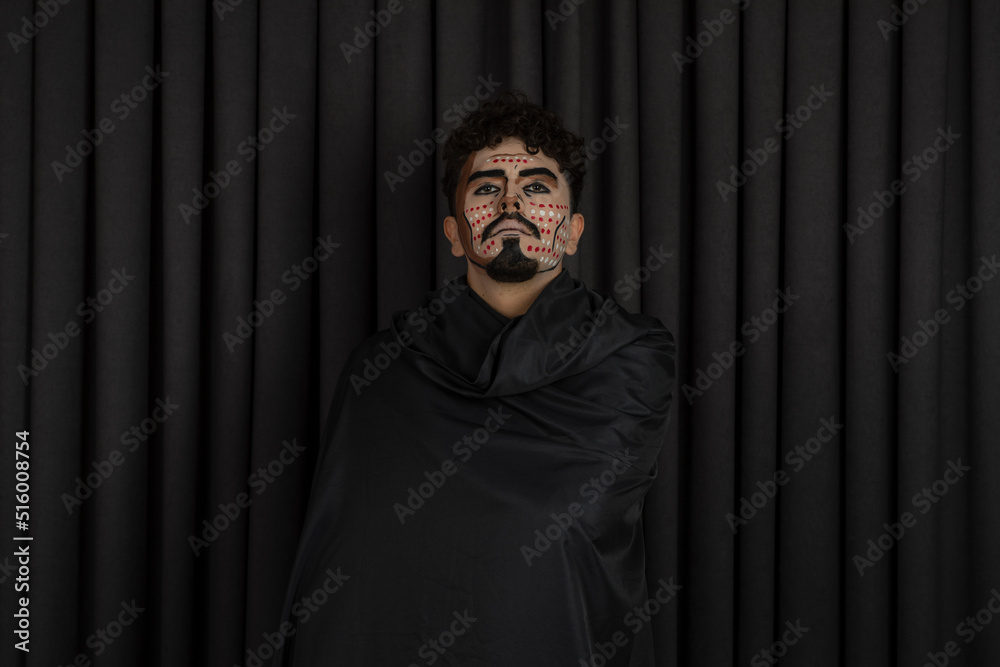 Confident young man with black cape stands on black background Confident young man with black cape stands on black background