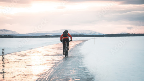 Mountain biker on ice skating track called "medvinden" on lake storsjön near Östersund (Sweden Lapland) riding towards mountain view during sunset.