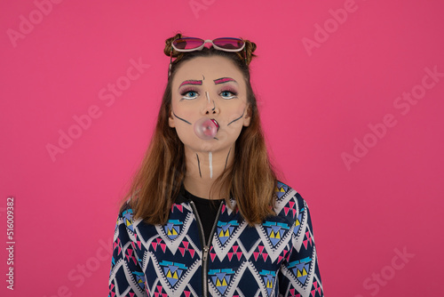 Close up portrait of young girl wearing creative makeup and making gum bubble