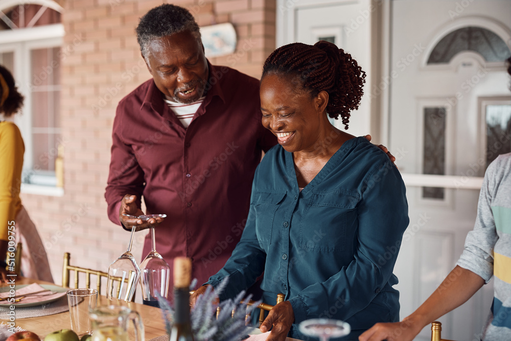 Happy senior black woman and her husband having fun while setting dining table for family lunch on patio. Happy senior black woman and her husband having fun while setting dining table for family lunch on patio.