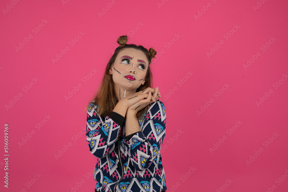 Portrait of young girl wearing colorful fantasy makeup and holding her hands together while looking aside