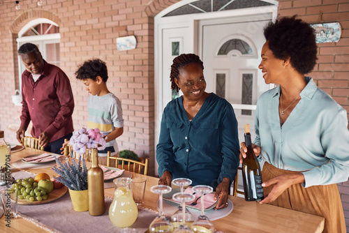 Happy black women talking while setting dining table for family lunch on patio.