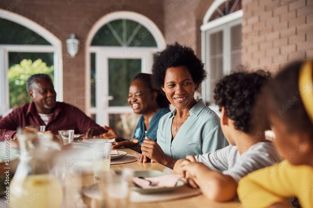 Happy African American woman talks to her kids during family meal at dining table on patio. Happy African American woman talks to her kids during family meal at dining table on patio.