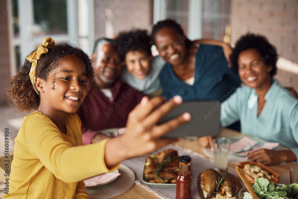 Fototapeta premium Happy African American girl and her extended family taking selfie during meal on patio.