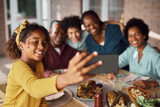 Happy African American girl and her extended family taking selfie during meal on patio.