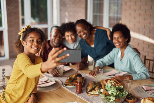 Happy black multi-generation family taking selfie during lunch at dining table.