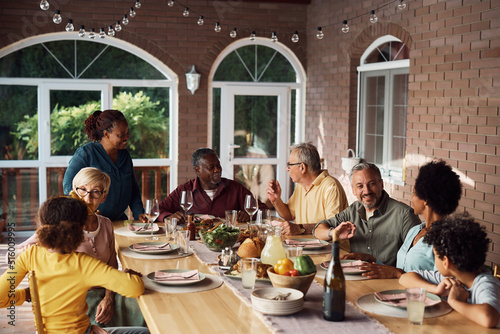 Happy multiethnic extended family talks during meal at dining table on patio.