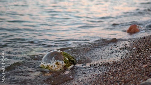 Calm waves at Giardini Naxos Beach, located on the coast of the Ionian Sea. Stone and sand shown from a low angle, with the background blurred. 
