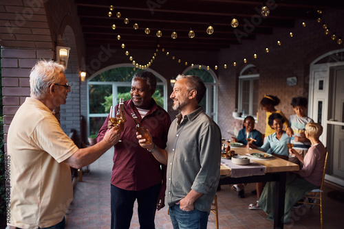 Group of multi-ethnic men toasting with drinks during family gathering on patio.