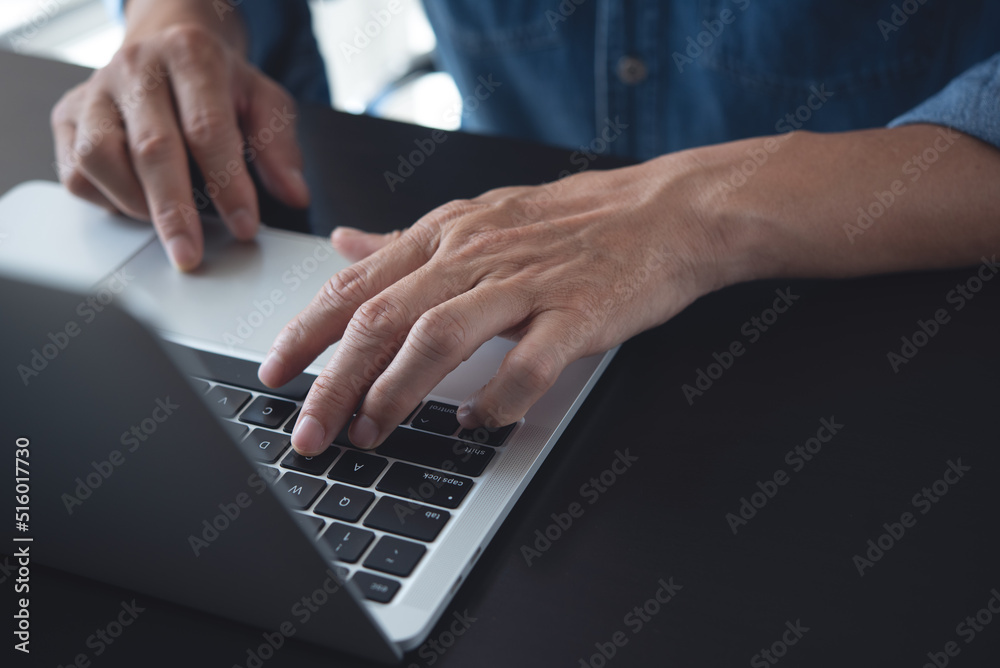 Closeup of a business man's hands working and typing on laptop computer keyboard on wooden table Closeup of a business man's hands working and typing on laptop computer keyboard on wooden table
