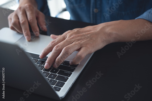 Closeup of a business man's hands working and typing on laptop computer keyboard on wooden table