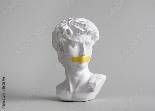 Michelangelo's David head bust in duct tape sealed mouth. Minimal concept on gray background censorship of freedom of speech and restrictions of thought and word. Fight for your rights.