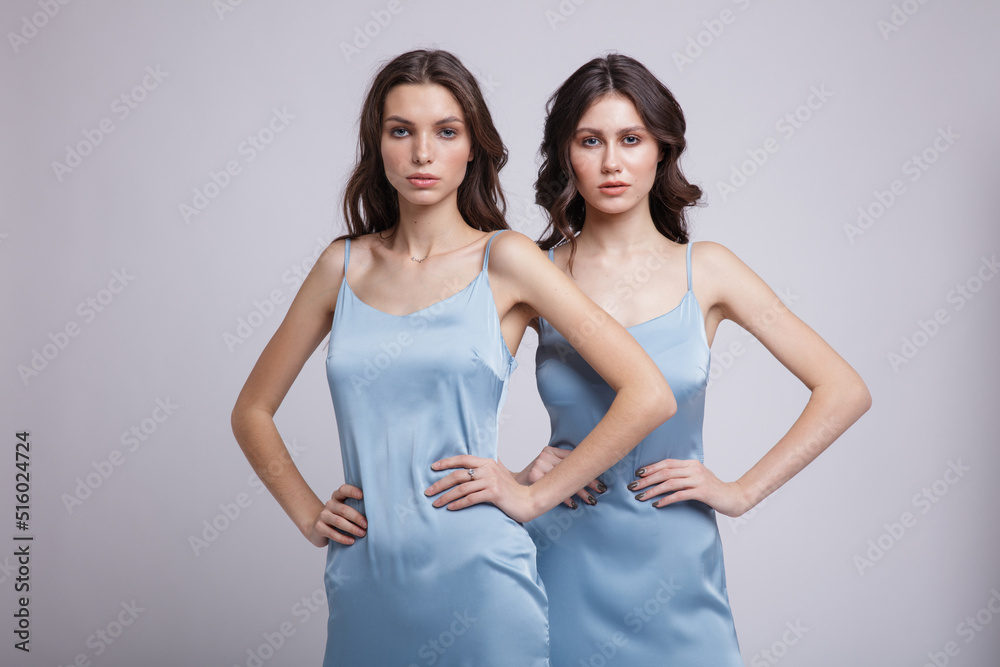 Two fashion models in same looks, outfits. Pretty sky blue dress. Beautiful young woman.  Girls posing on white studio background