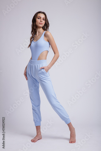 High fashion photo of a beautiful elegant young woman in a pretty blue body slim, pants posing on white background. Slim figure, studio shot. Brunette, long hair