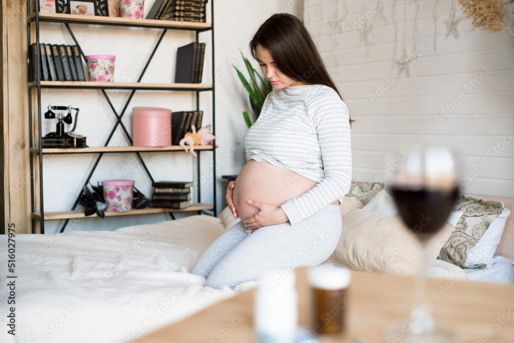 A glass of red wine and pills on the background of a pregnant woman. Alcoholic concept. A glass of red wine and pills on the background of a pregnant woman. Alcoholic concept.